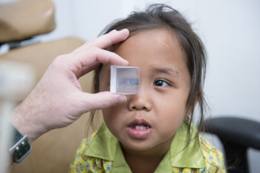 Young girl in green and yellow shirt being tested for Strabismus using a prism
