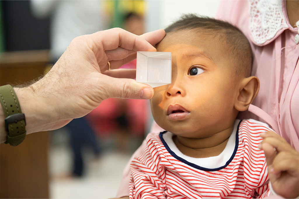 Young child in red and white shirt being tested for a refractive error