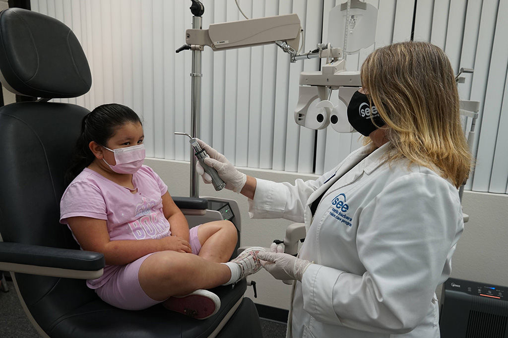 Female eye doctor providing free eye exam to a young girl sitting in a chair at a SEE Vision Care office